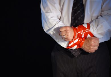 A close up of a man in a suite with his hands tied up with red tape